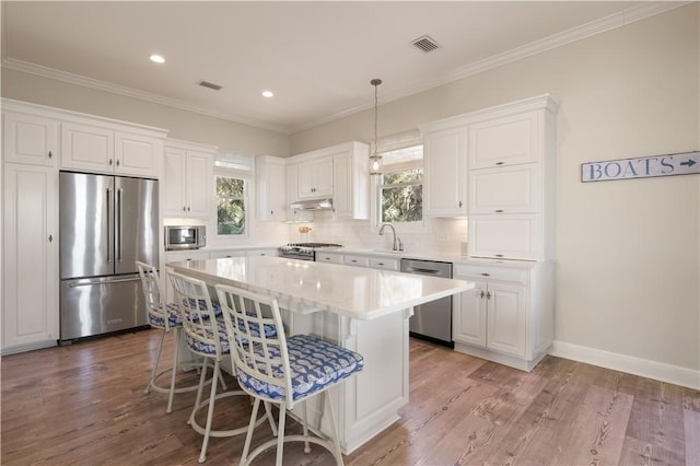 kitchen featuring white cabinets, appliances with stainless steel finishes, a center island, and wood-type flooring