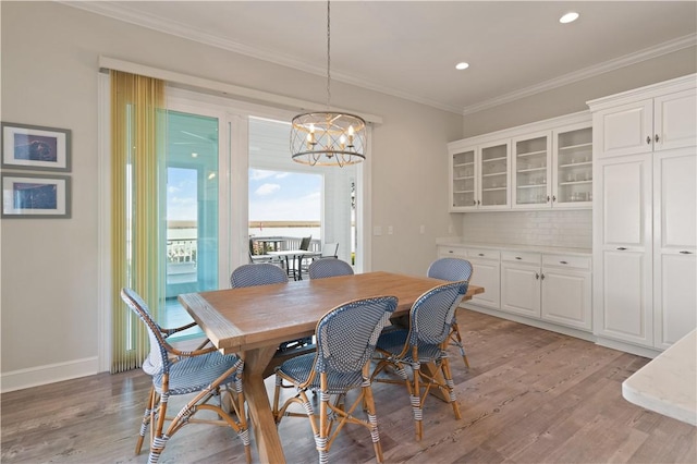 dining space with ornamental molding, light wood-type flooring, and a notable chandelier