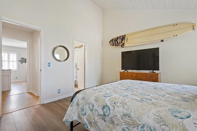 bedroom with hardwood / wood-style flooring, ensuite bathroom, and vaulted ceiling