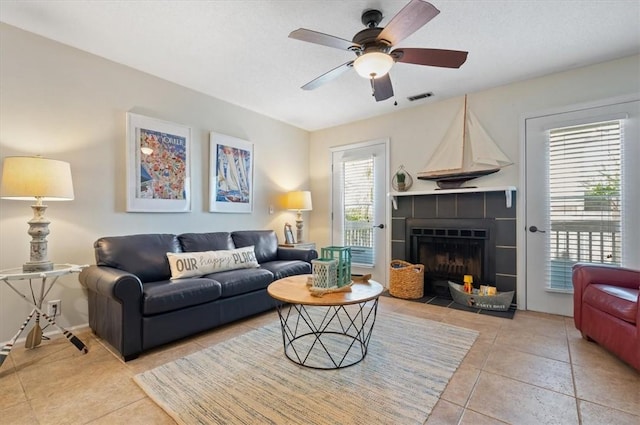 living room featuring a tiled fireplace, light tile patterned floors, and ceiling fan