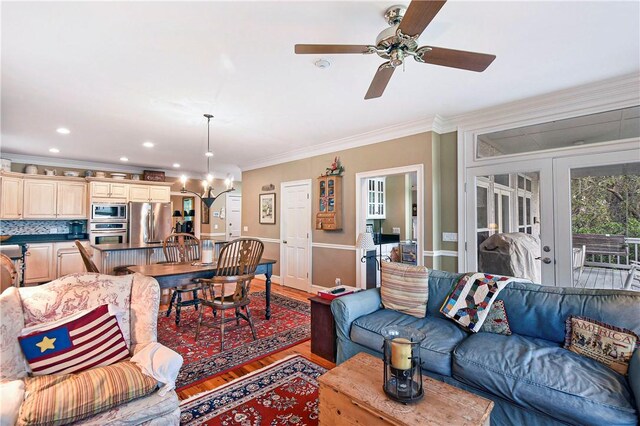 living room with crown molding, light hardwood / wood-style flooring, ceiling fan with notable chandelier, and french doors