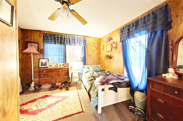 bedroom with carpet, ceiling fan, a textured ceiling, and wooden walls