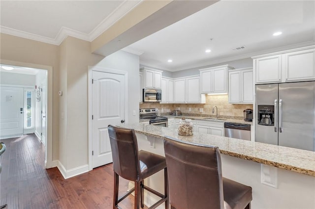 kitchen featuring a kitchen breakfast bar, light stone counters, dark hardwood / wood-style flooring, white cabinets, and appliances with stainless steel finishes