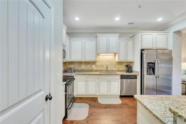 kitchen with sink, white cabinetry, light stone counters, wood-type flooring, and stainless steel appliances