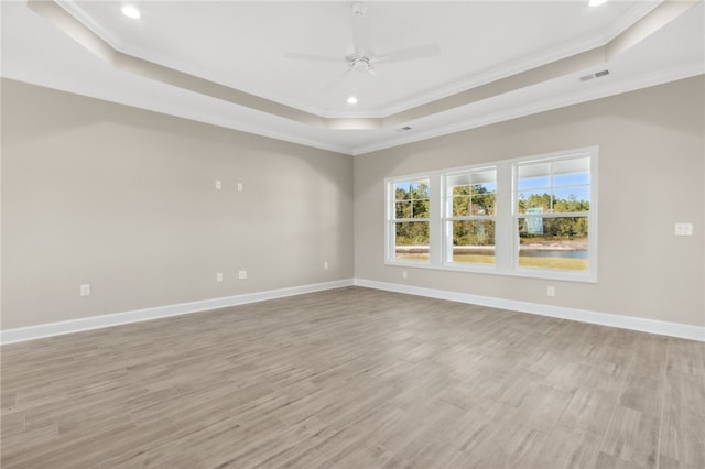 unfurnished room with a tray ceiling, ornamental molding, and light wood-type flooring