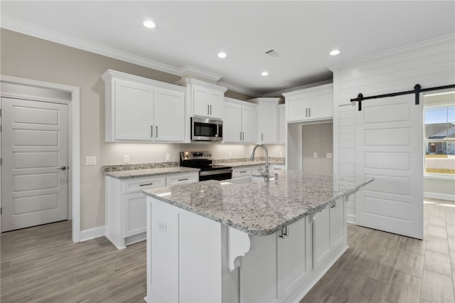 kitchen with white cabinetry, a kitchen island with sink, a barn door, sink, and appliances with stainless steel finishes