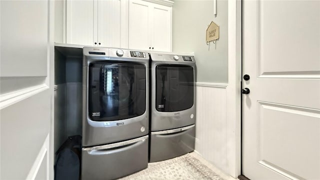 clothes washing area with cabinet space, separate washer and dryer, and wainscoting