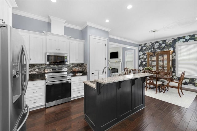 kitchen featuring appliances with stainless steel finishes, ornamental molding, a sink, a kitchen bar, and white cabinetry