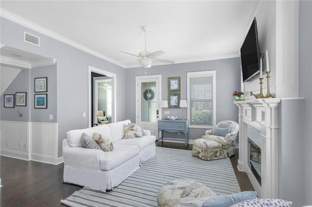 living area with dark wood finished floors, a glass covered fireplace, a ceiling fan, crown molding, and baseboards