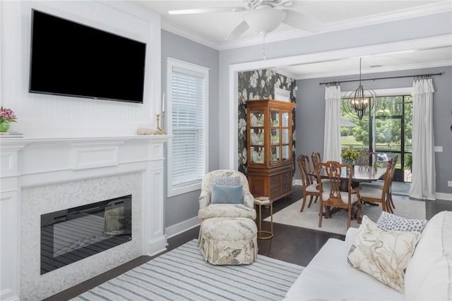 living room featuring a chandelier, a glass covered fireplace, a ceiling fan, wood finished floors, and baseboards