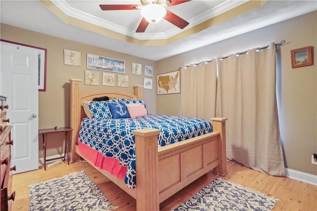 bedroom with a tray ceiling, baseboards, wood finished floors, and crown molding