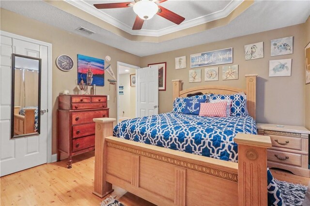 bedroom featuring visible vents, light wood-style floors, a tray ceiling, and ornamental molding