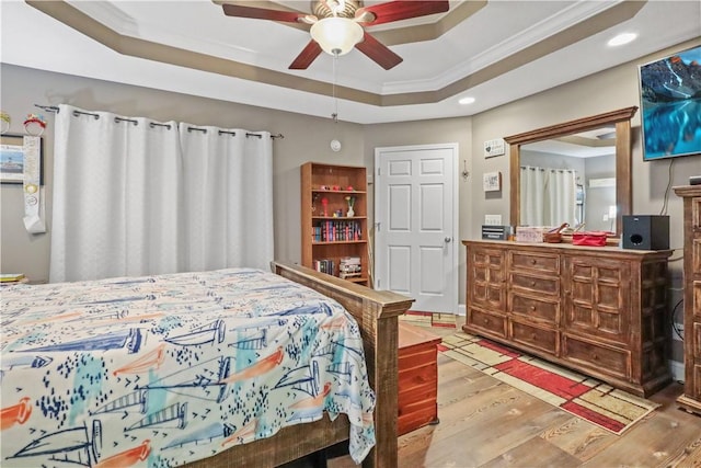 bedroom with ornamental molding, a ceiling fan, a tray ceiling, wood finished floors, and recessed lighting