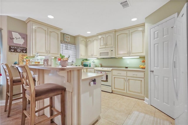 kitchen with visible vents, cream cabinetry, white appliances, a breakfast bar area, and light countertops