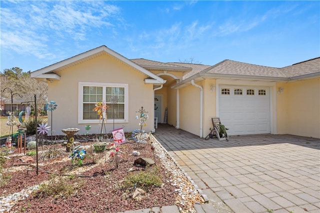 ranch-style house featuring stucco siding, an attached garage, a shingled roof, and decorative driveway