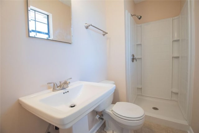 bathroom with toilet, tiled shower, and a sink