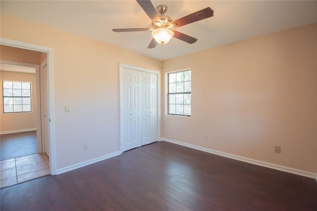 unfurnished bedroom with a closet, a ceiling fan, dark wood-type flooring, and baseboards