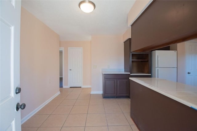 kitchen featuring baseboards, light tile patterned flooring, light countertops, and freestanding refrigerator