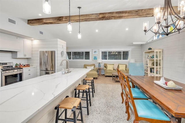 kitchen featuring sink, white cabinetry, stainless steel appliances, light stone counters, and decorative light fixtures