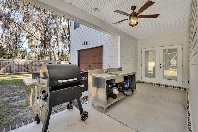 view of patio featuring fence, a sink, ceiling fan, french doors, and a garage