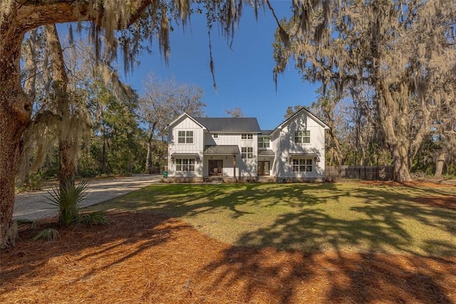 traditional home featuring board and batten siding, fence, a front yard, metal roof, and driveway