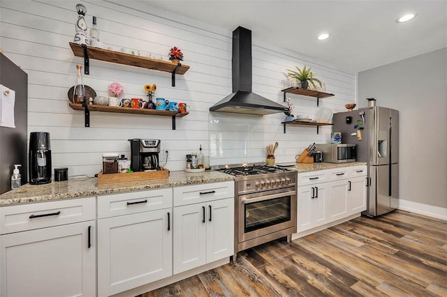 kitchen featuring dark wood-type flooring, light stone counters, stainless steel appliances, wall chimney exhaust hood, and open shelves