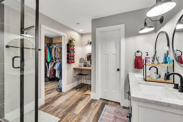 full bathroom with a walk in closet, double vanity, a stall shower, wood finished floors, and a sink