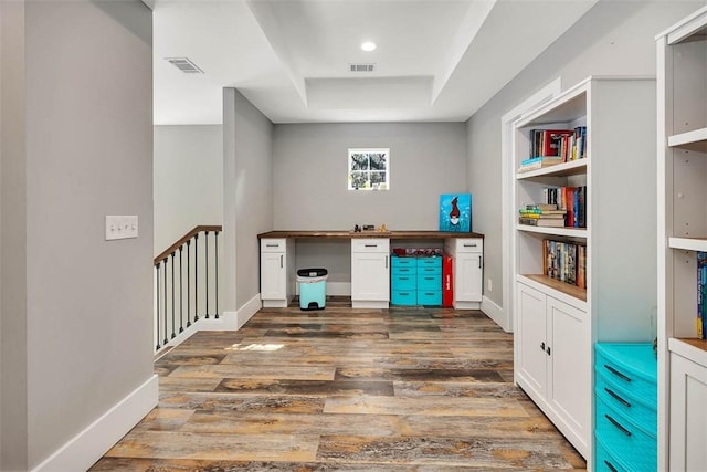 office area featuring visible vents, built in study area, a raised ceiling, and wood finished floors