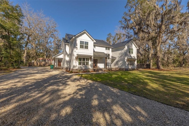 view of front of property with gravel driveway, a front lawn, board and batten siding, and metal roof