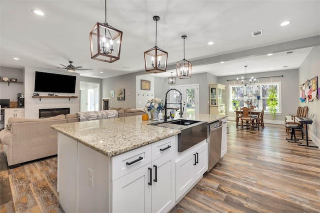 kitchen featuring wood finished floors, a kitchen island with sink, a sink, dishwasher, and ceiling fan with notable chandelier