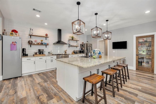 kitchen featuring a sink, open shelves, freestanding refrigerator, light wood-style floors, and wall chimney exhaust hood