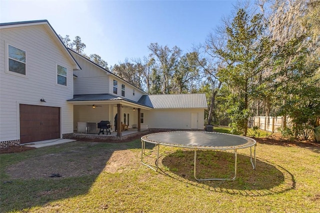 rear view of house with a trampoline, fence, an attached garage, a ceiling fan, and a patio