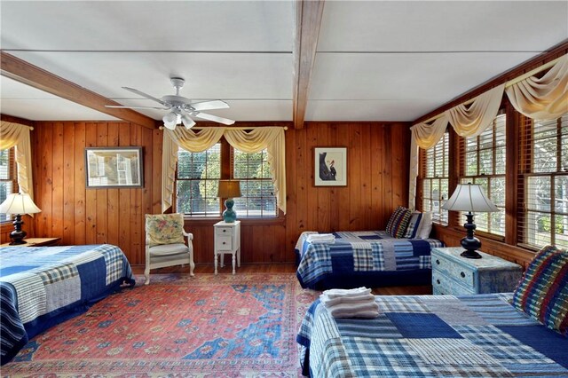 bedroom with beamed ceiling, multiple windows, wooden walls, and ceiling fan