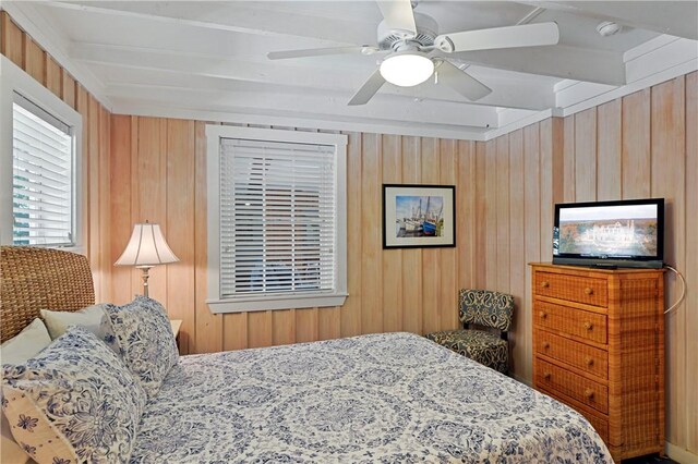 bedroom with beam ceiling, ceiling fan, and wooden walls