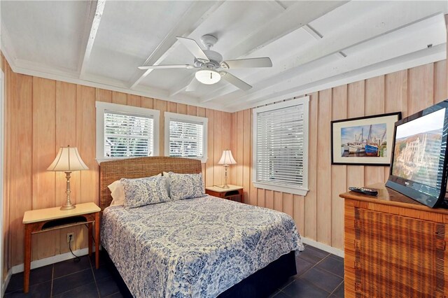 bedroom with ceiling fan, wooden walls, dark tile patterned floors, and beamed ceiling