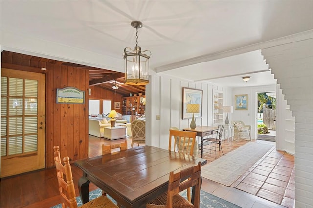 dining space featuring wood walls, hardwood / wood-style floors, ceiling fan, and lofted ceiling with beams