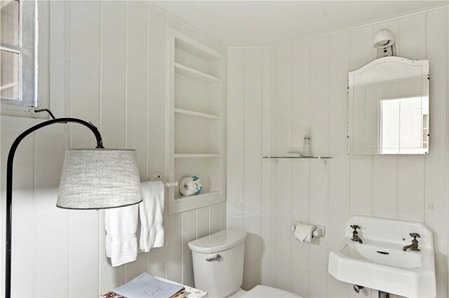 bathroom featuring built in shelves, wood walls, sink, and toilet