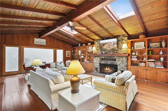 living room featuring wood walls, lofted ceiling with skylight, a stone fireplace, light hardwood / wood-style flooring, and ceiling fan