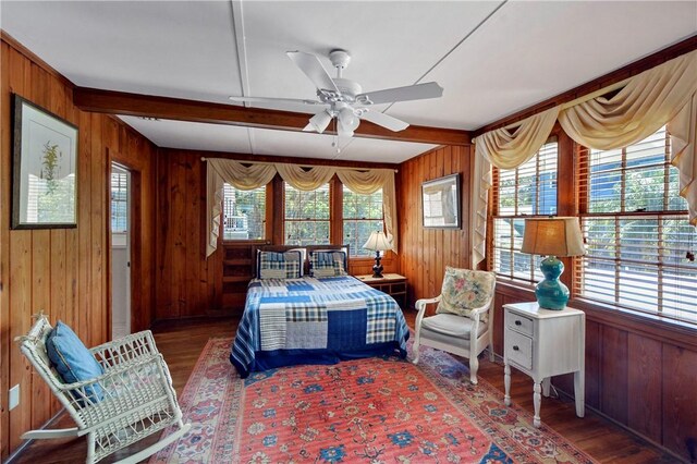 bedroom featuring ceiling fan, beam ceiling, dark wood-type flooring, and wooden walls