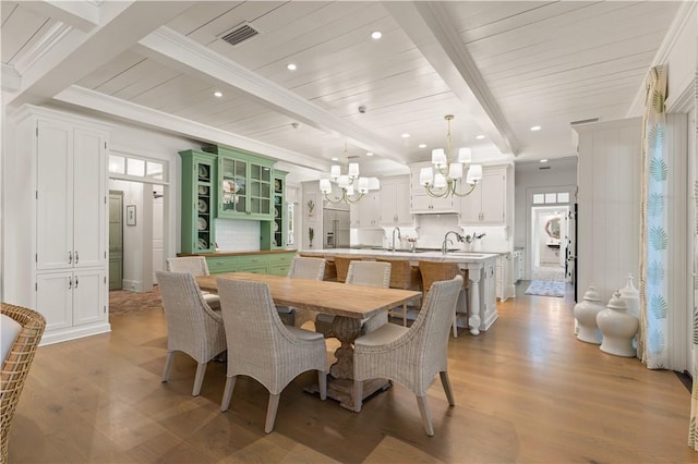 dining area with beamed ceiling, light wood-type flooring, sink, and a chandelier