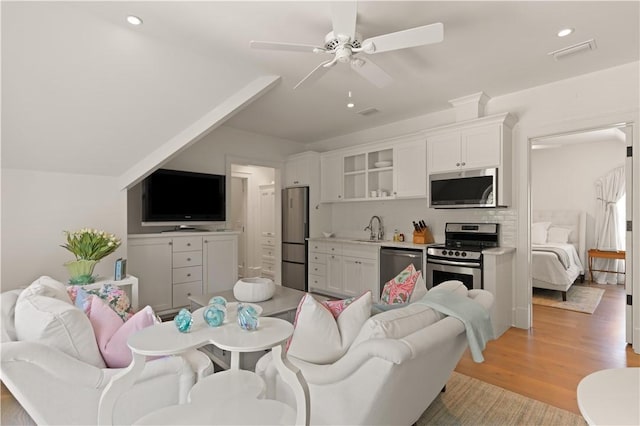 living room featuring ceiling fan, sink, light hardwood / wood-style floors, and vaulted ceiling