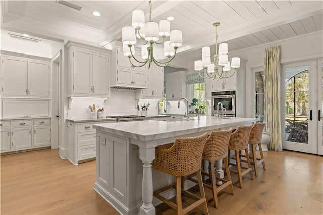 kitchen with a center island with sink, pendant lighting, white cabinetry, and light hardwood / wood-style flooring