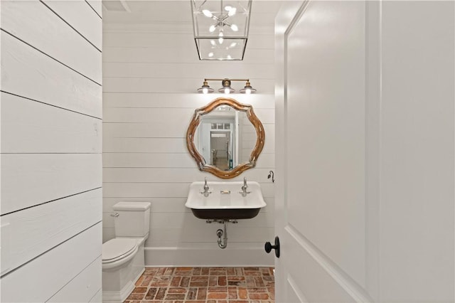 bathroom with wood walls, sink, and toilet