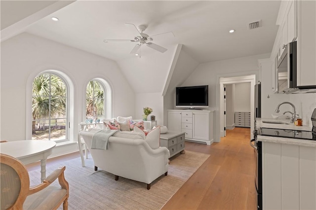 living room with ceiling fan, light hardwood / wood-style floors, sink, and vaulted ceiling