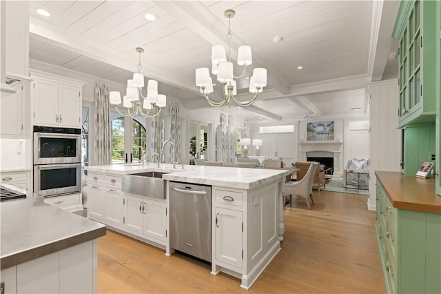 kitchen with appliances with stainless steel finishes, a kitchen island with sink, pendant lighting, beam ceiling, and white cabinetry