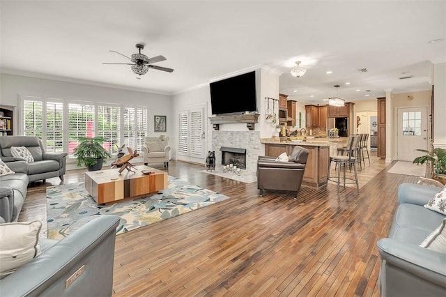 living room featuring dark hardwood / wood-style floors, a stone fireplace, ceiling fan, and crown molding