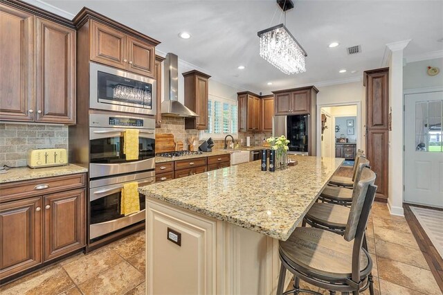 kitchen featuring appliances with stainless steel finishes, ornamental molding, wall chimney exhaust hood, pendant lighting, and a center island