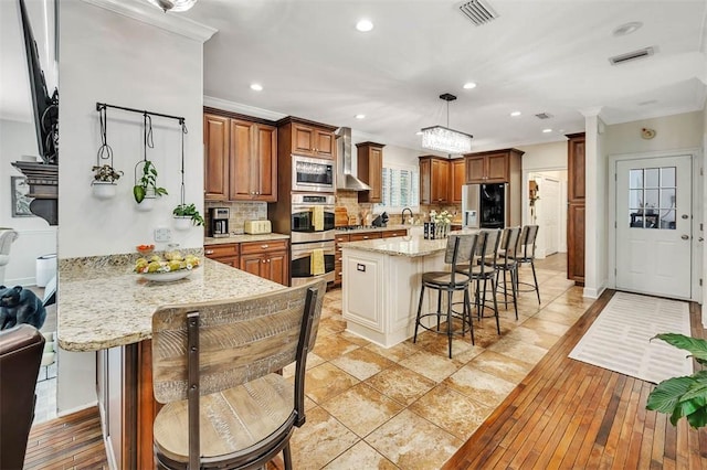 kitchen featuring a kitchen breakfast bar, backsplash, pendant lighting, light wood-type flooring, and appliances with stainless steel finishes