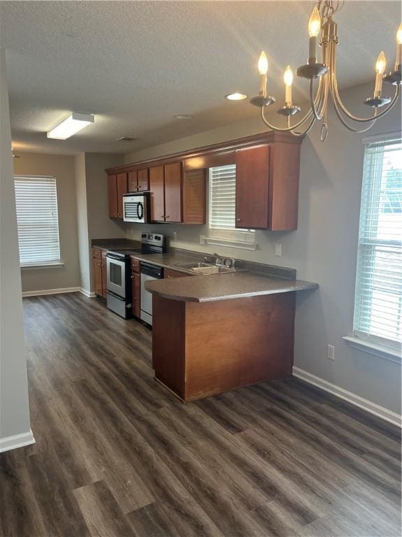 kitchen featuring appliances with stainless steel finishes, decorative light fixtures, sink, dark hardwood / wood-style flooring, and kitchen peninsula