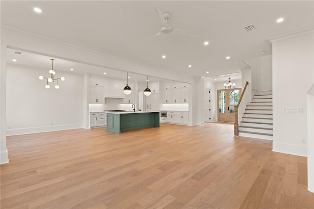 unfurnished living room featuring ornamental molding, sink, ceiling fan with notable chandelier, and light hardwood / wood-style flooring